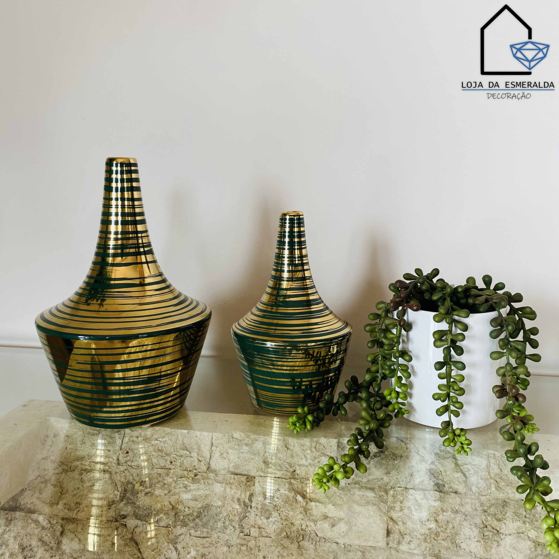 Dois jarros cerâmicos decorativos dourados e negros com vaso branco e planta suculenta pendente numa superfície de pedra