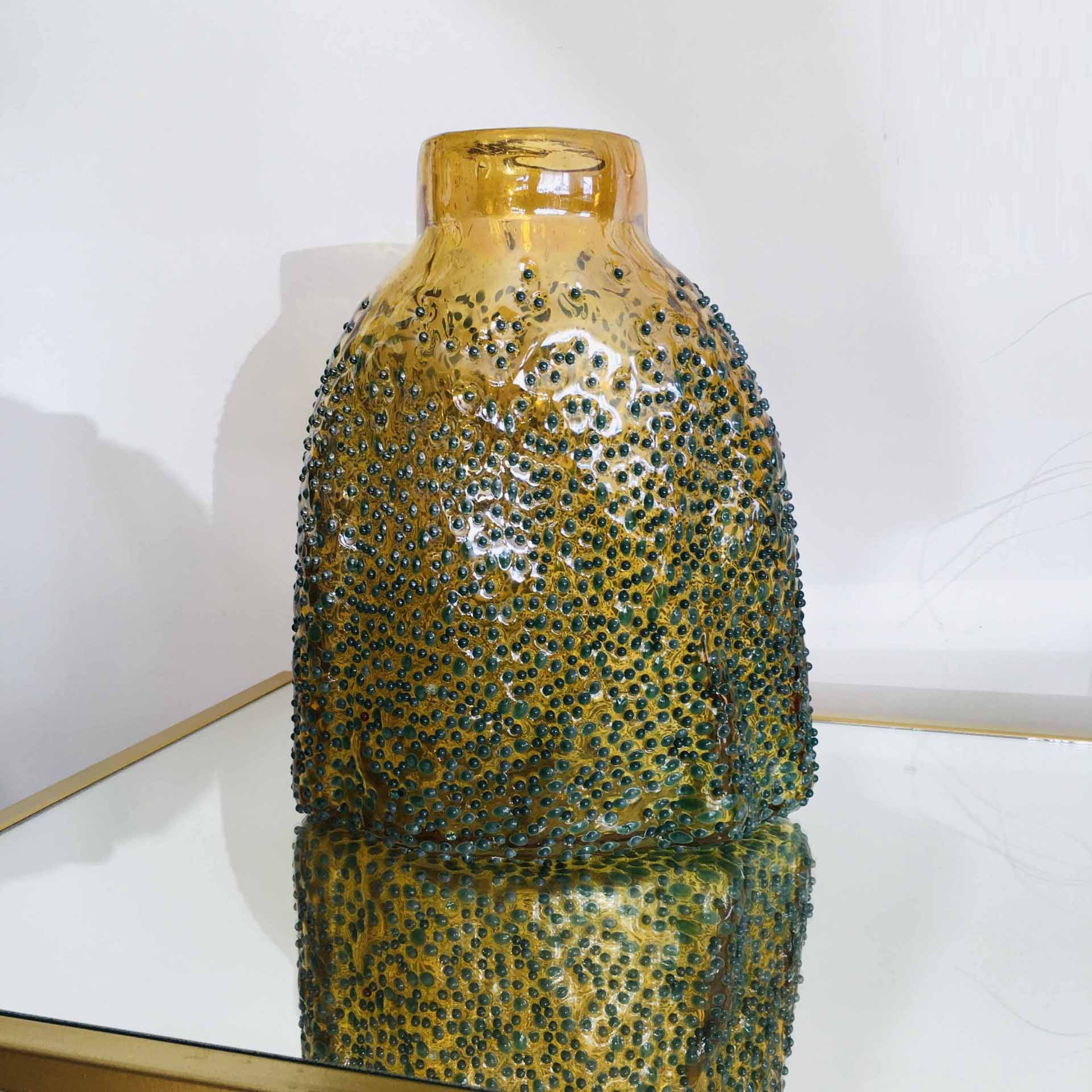 Vaso de vidro amarelo texturizado com relevo verde sobre espelho