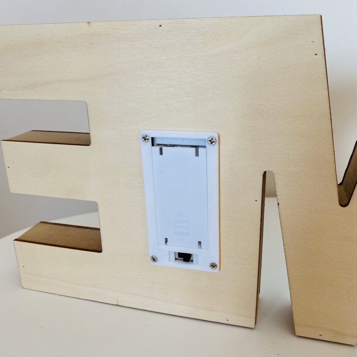 Letra decorativa em madeira clara com caixa para bateria na parte traseira