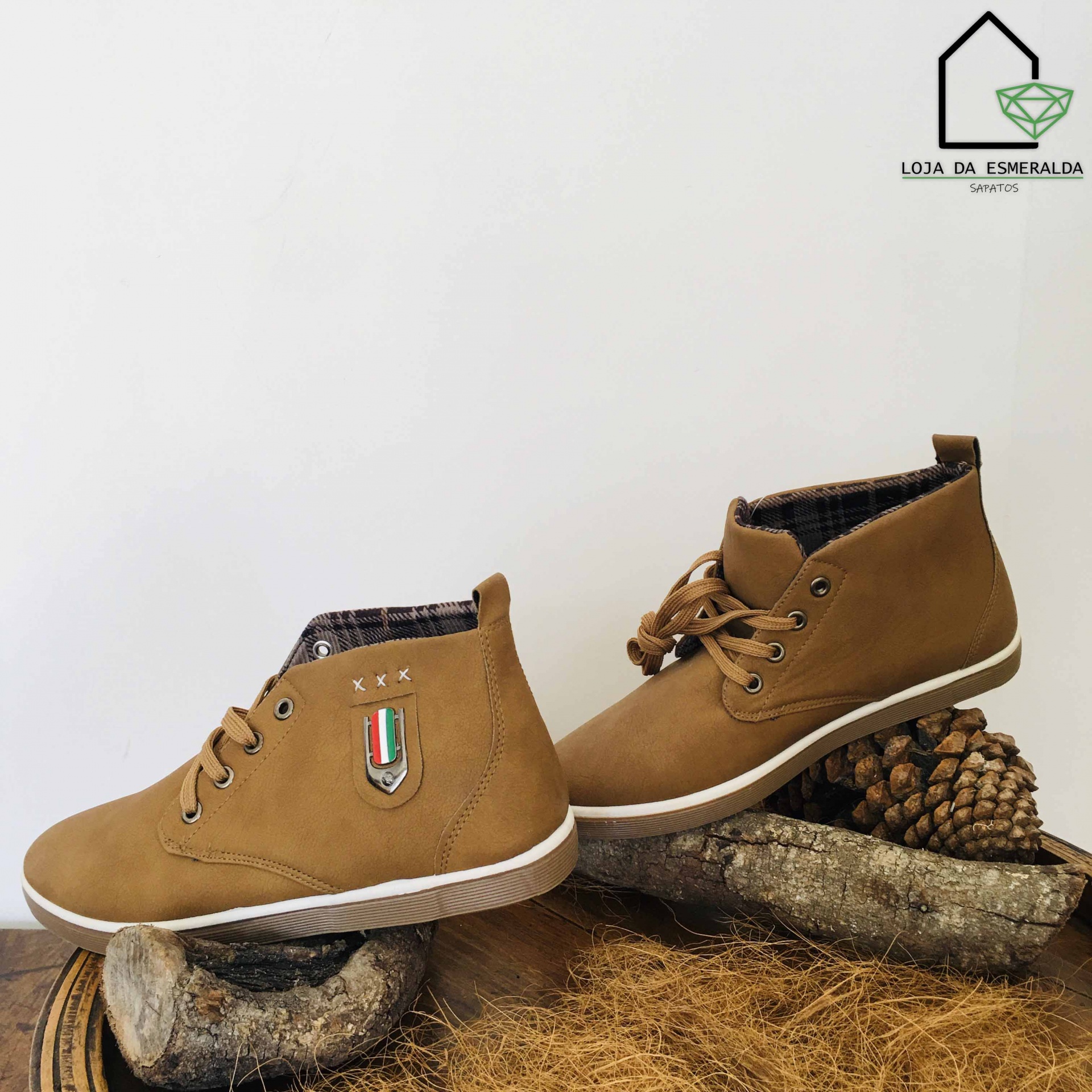 Tênis castanhos claros com sola branca e detalhes xadrez, sobre madeira e cones de pinheiro.