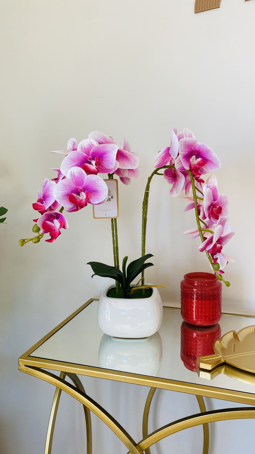 Orquídea artificial rosa em vaso branco sobre mesa com vidro espelhado e estrutura dourada