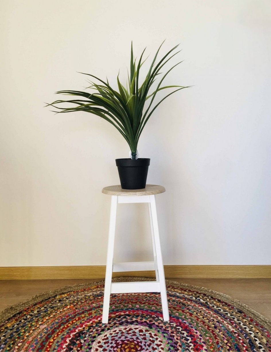 Planta artificial em vaso preto sobre banquinho branco e tapete colorido