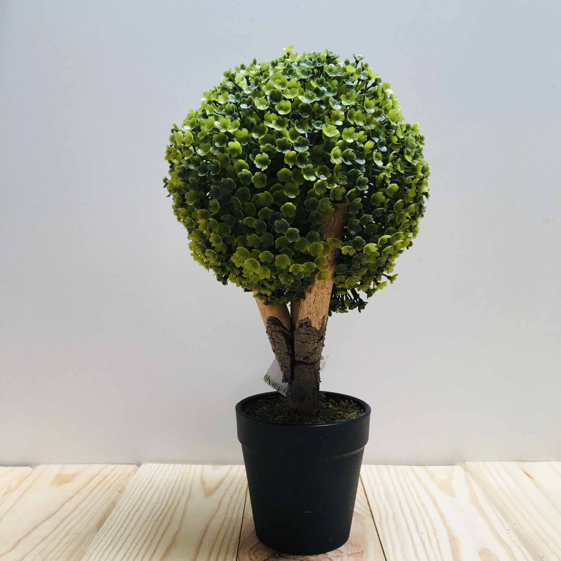 Árvore artificial em vaso preto sobre superfície de madeira clara