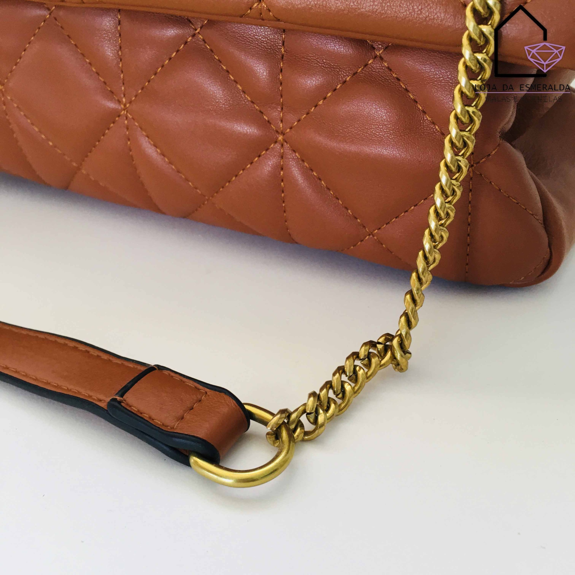 Mala de mão castanha com padrão acolchoado, alça dourada e parte em pele sobre fundo branco.