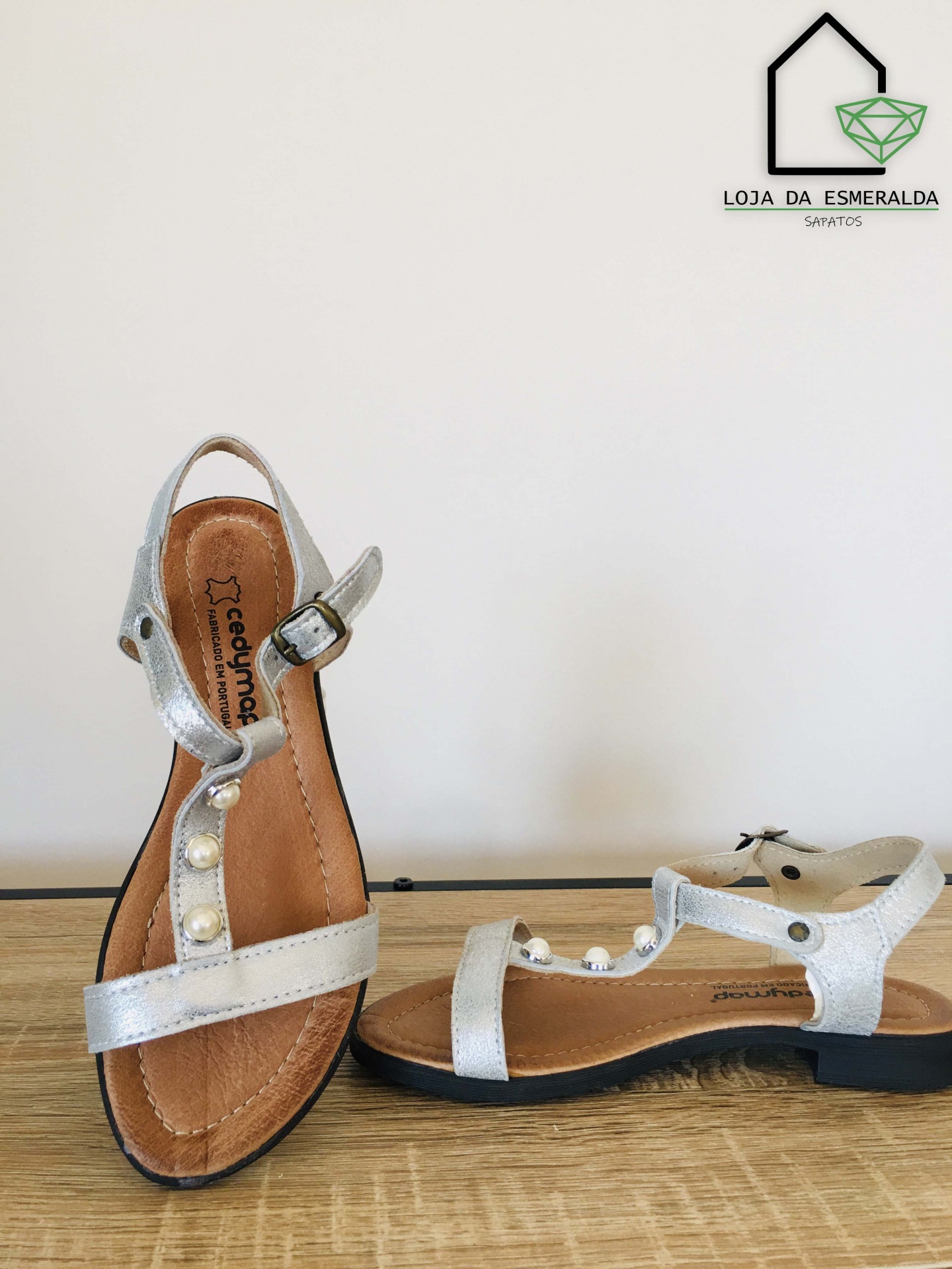 Sandálias prateadas com pérolas e sola preta em superfície de madeira clara