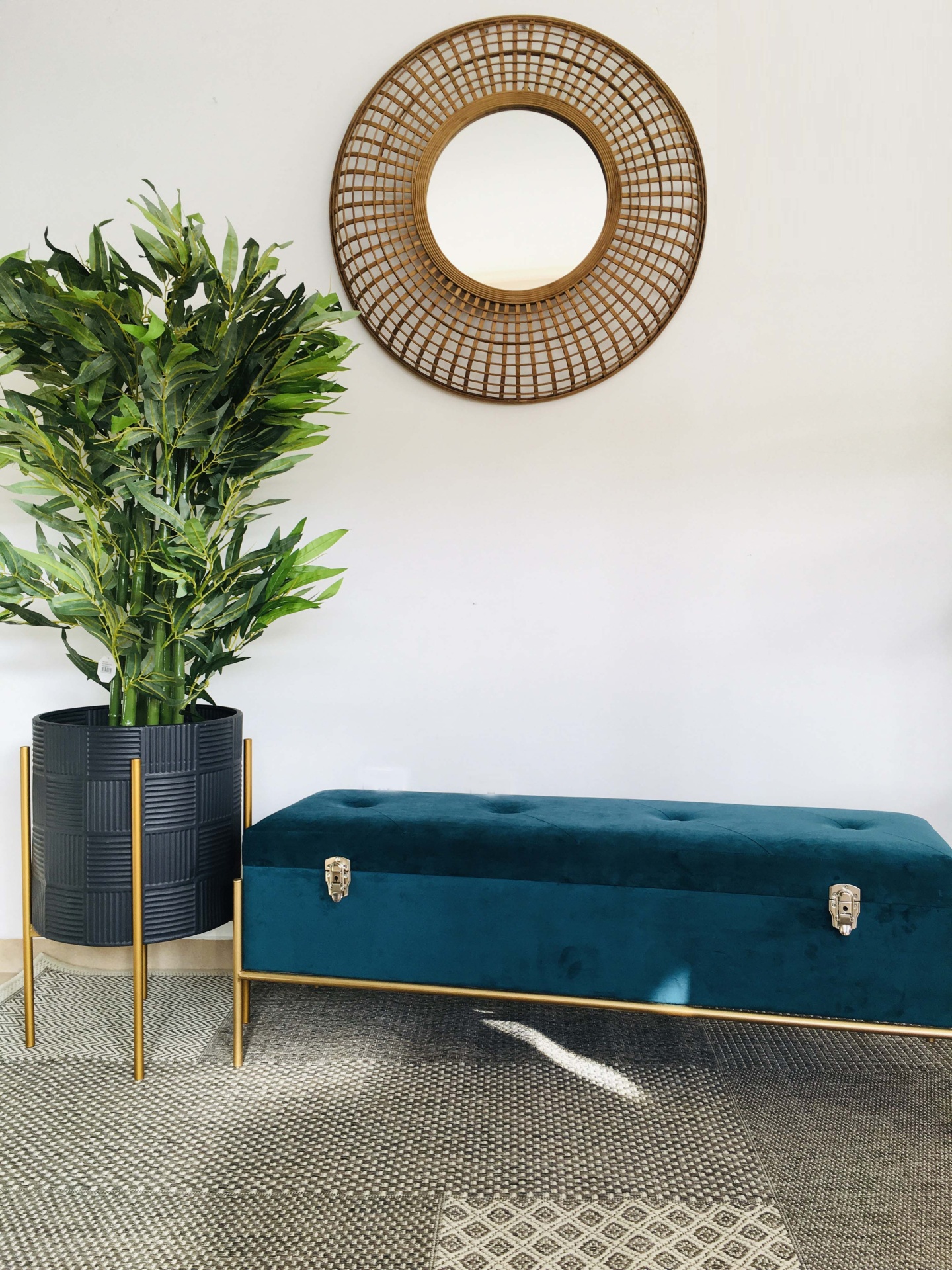 banco azul estofado com pés dourados, planta em vaso preto com suporte dourado e espelho redondo em parede branca