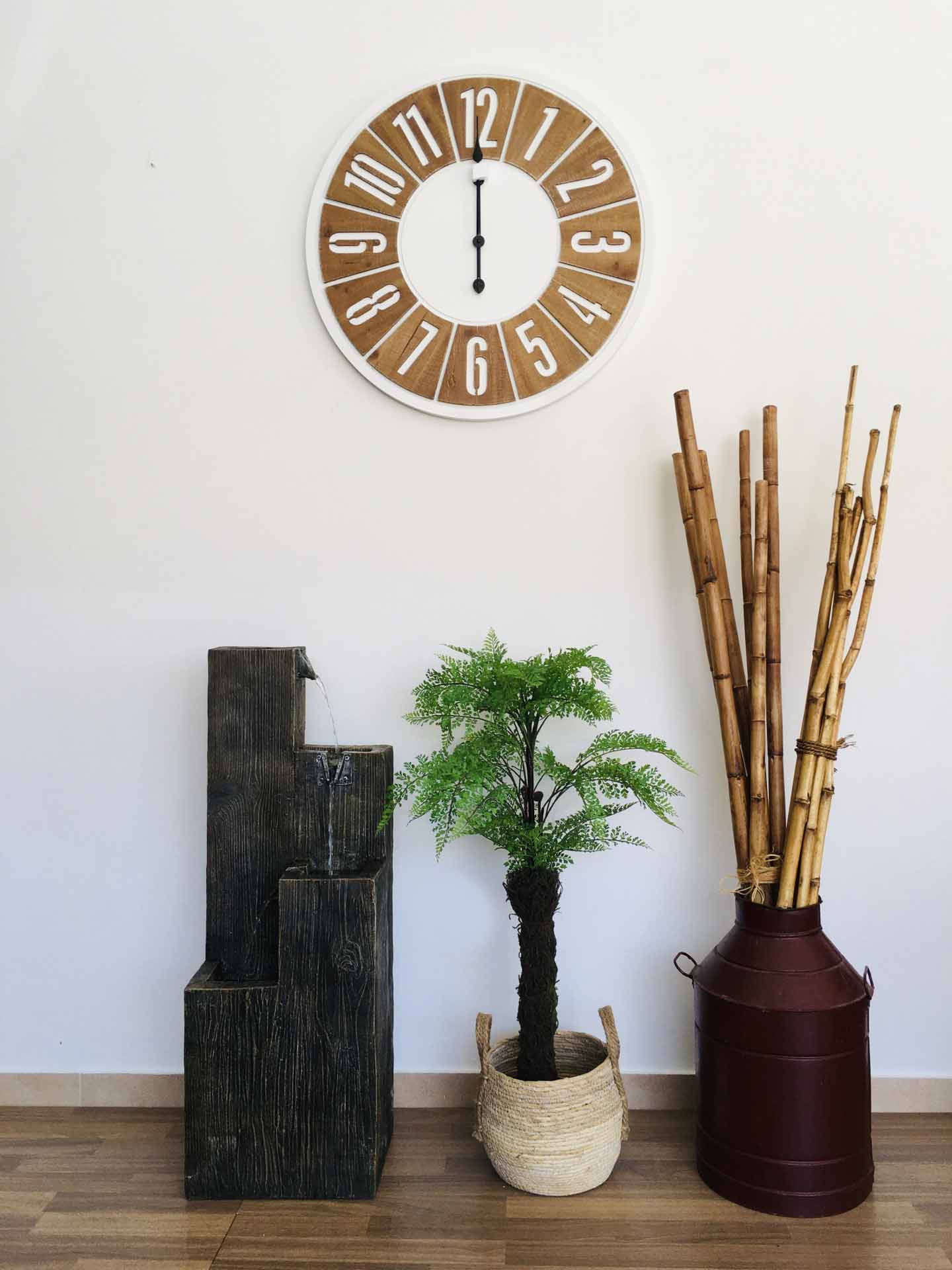 Relógio de parede com números brancos em madeira, fonte preta, planta verde em vaso trançado e jarro vermelho com bambus