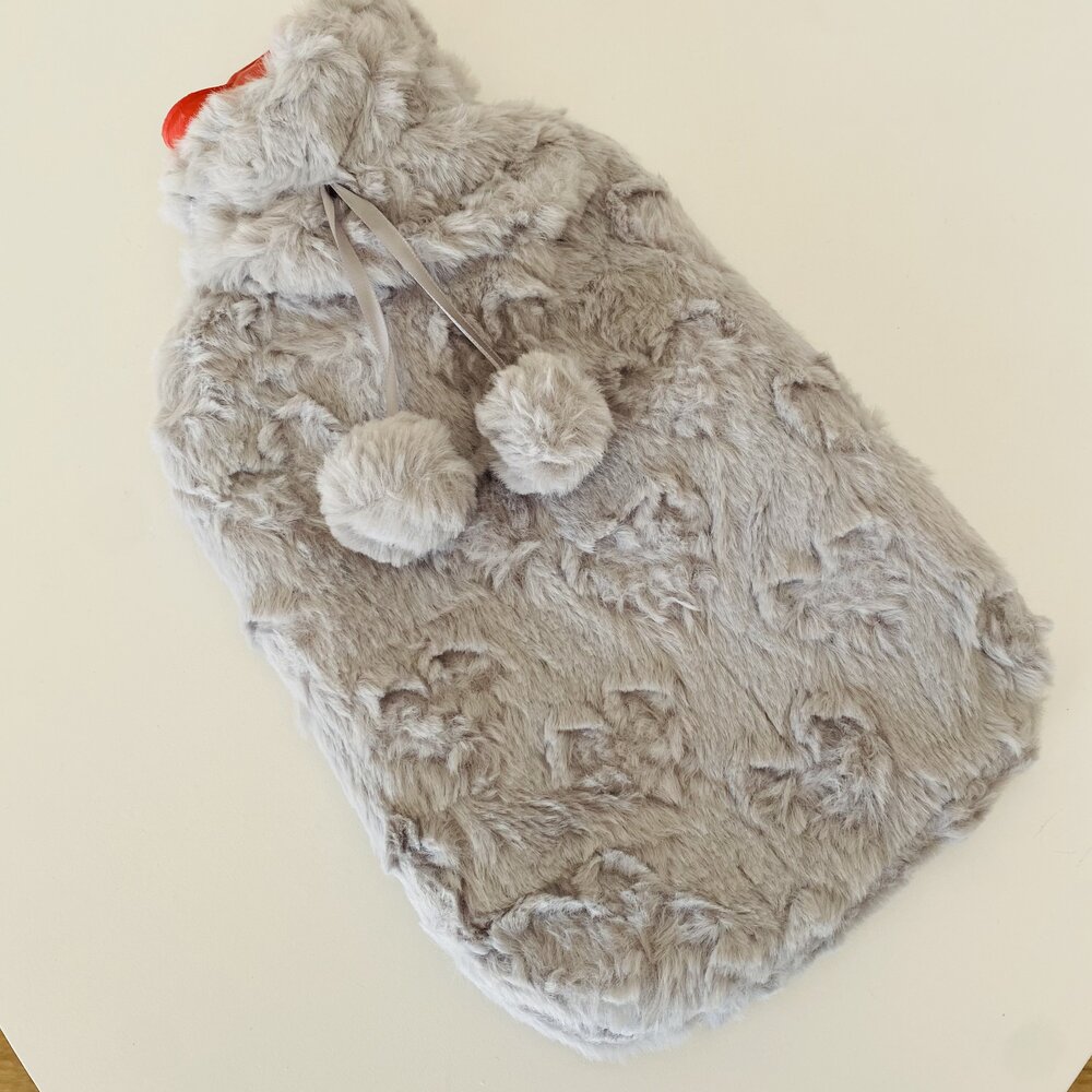 Frasco de água quente com cobertura cinzenta peluda e pompons.
