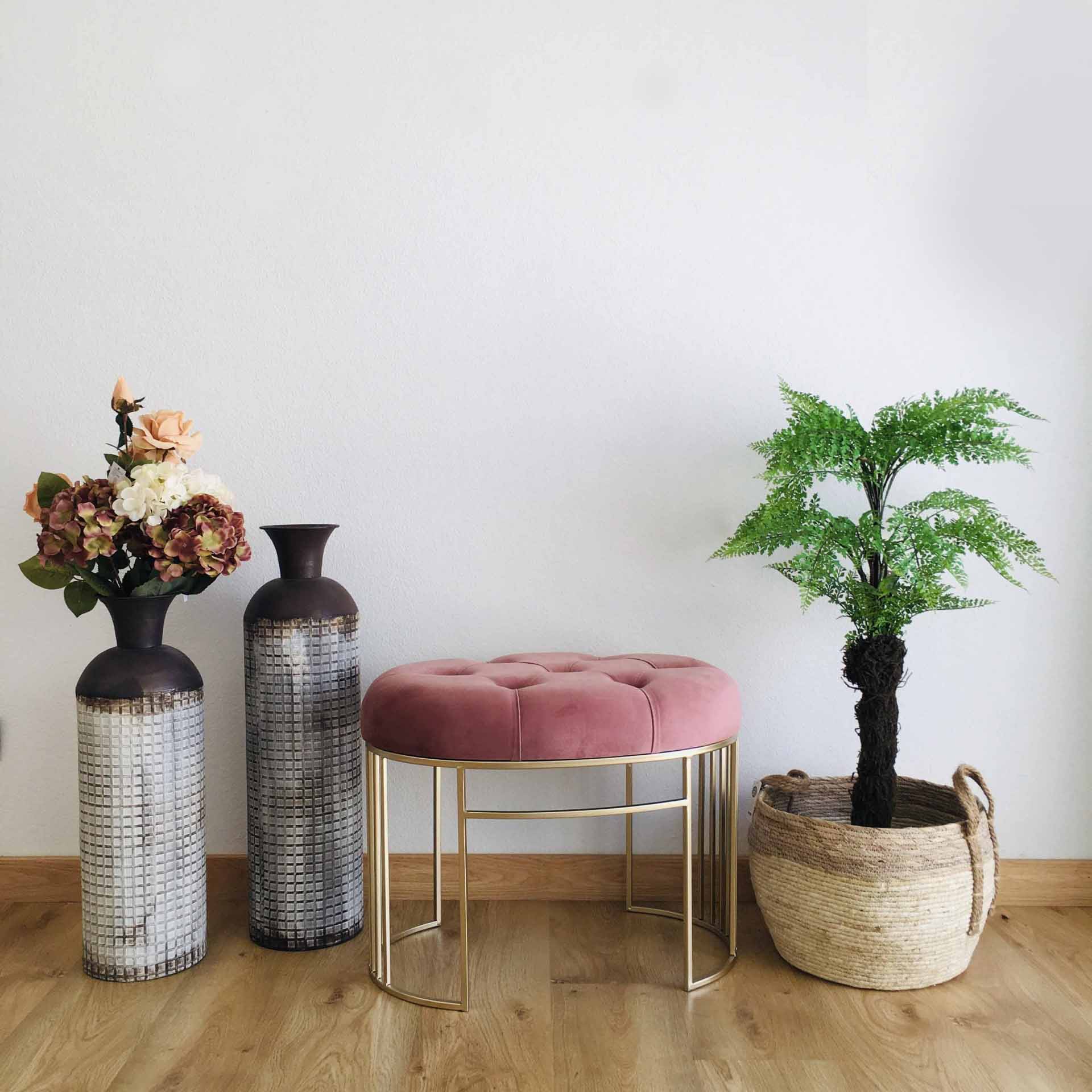 Banco rosa com pés dourados entre vasos com flores e planta