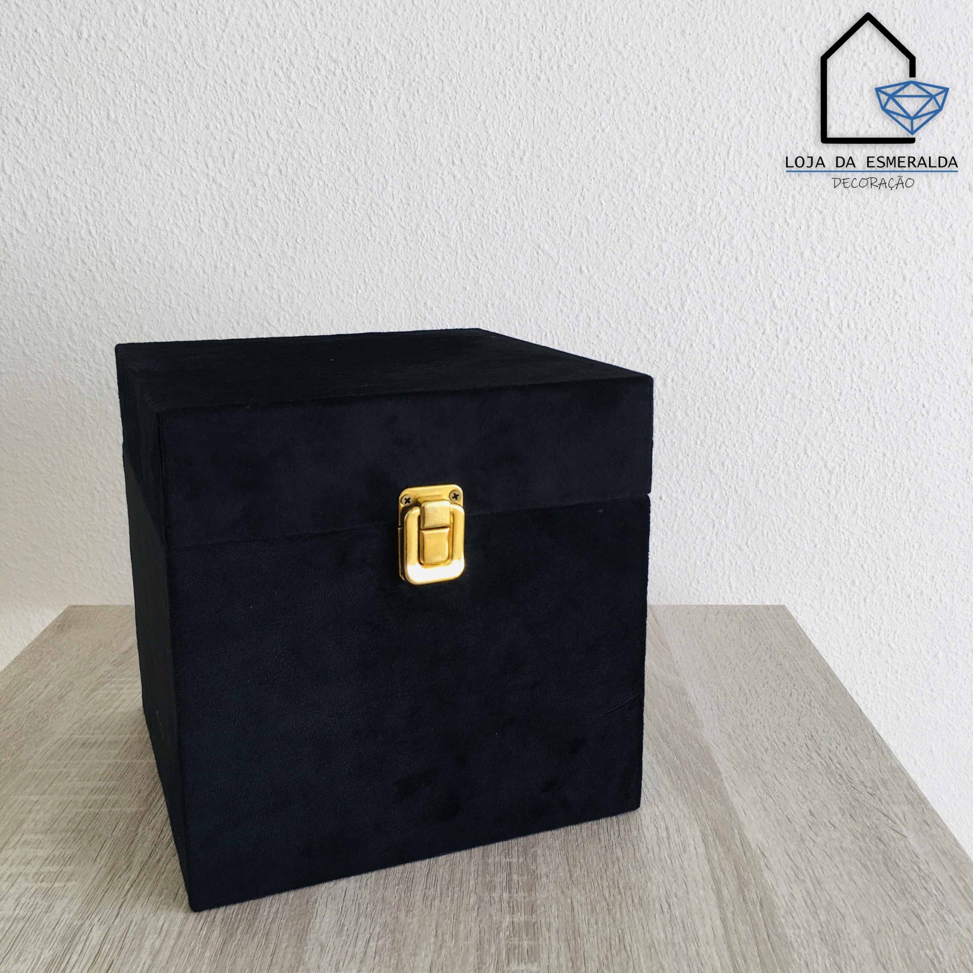 Caixa preta aveludada com fecho dourado sobre mesa de madeira clara