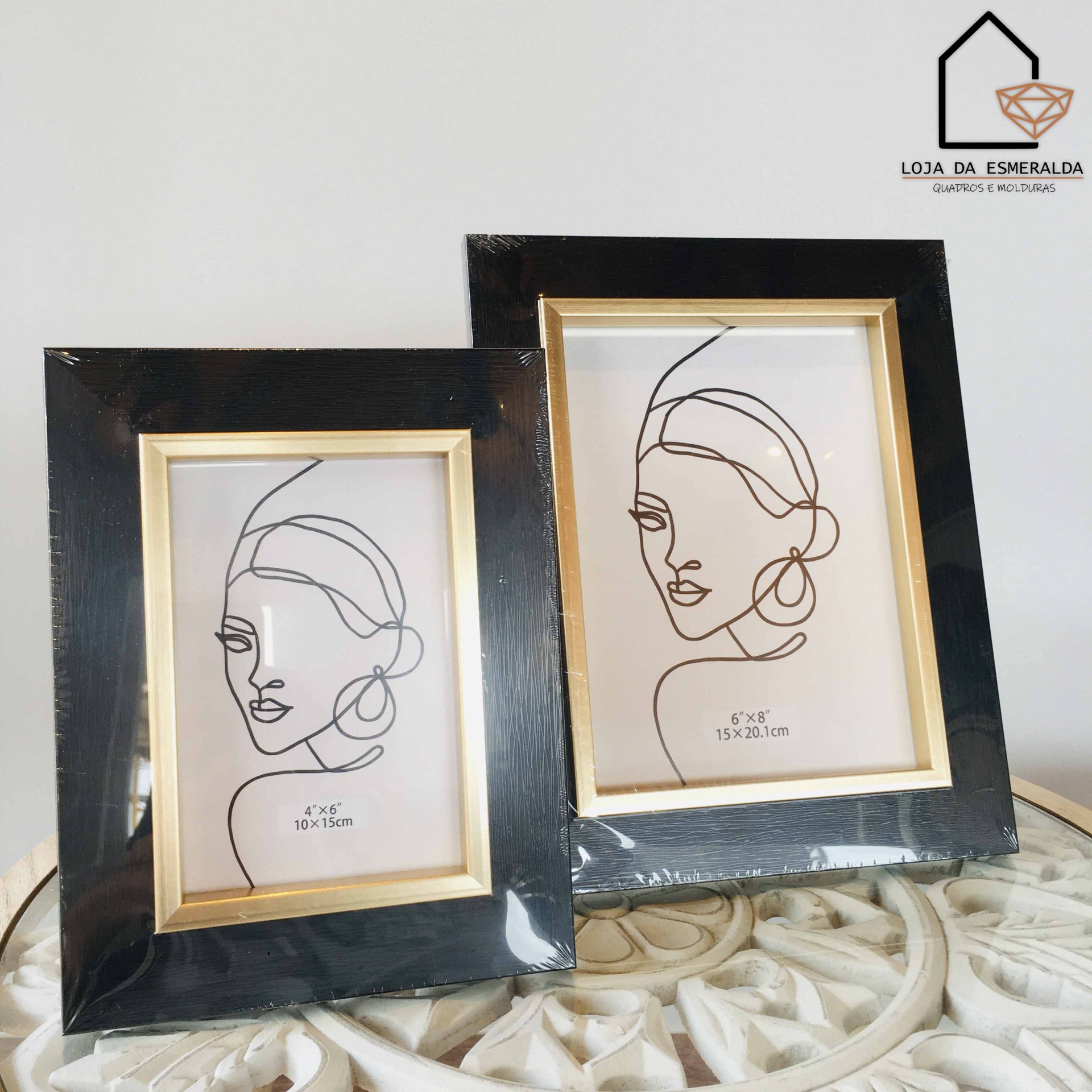 Dois porta-retratos pretos com borda dourada e desenhos de rostos femininos em linhas simples