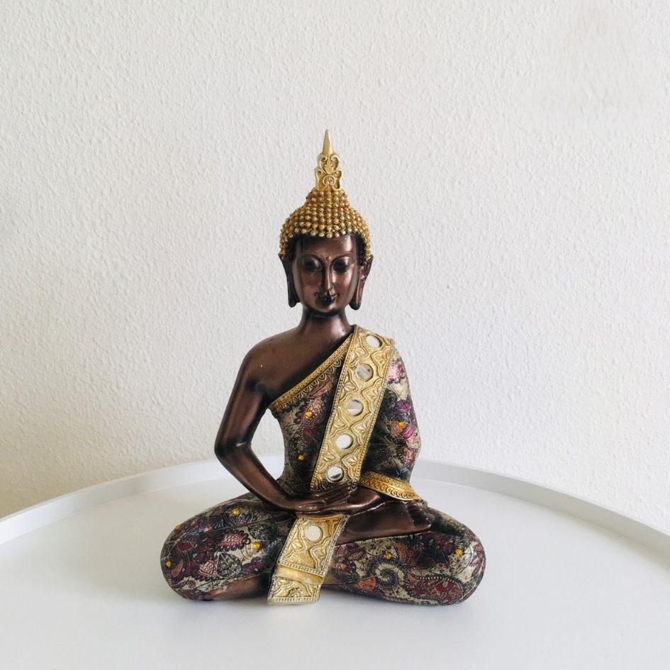 Estátua decorativa de Buda sentado com detalhes dourados e padrão floral colorido.
