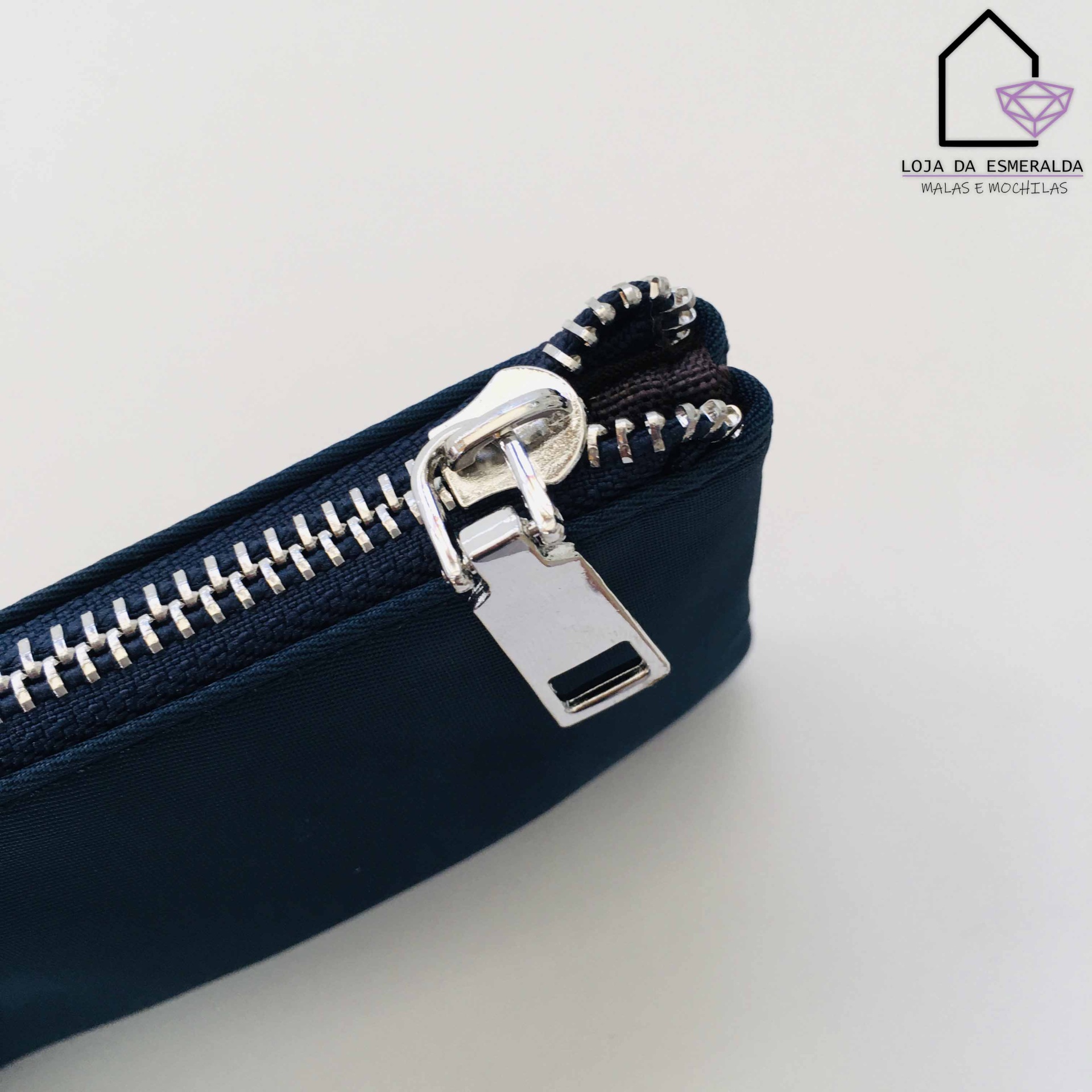 Fecho de correr metálico prateado em tecido azul escuro, com logotipo loja da esmeralda