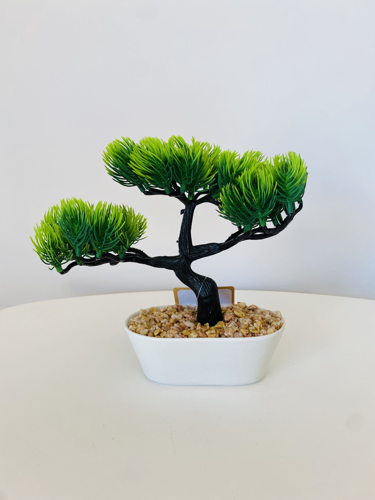 Árvore de bonsai artificial num vaso branco com pedras decorativas sobre uma mesa branca