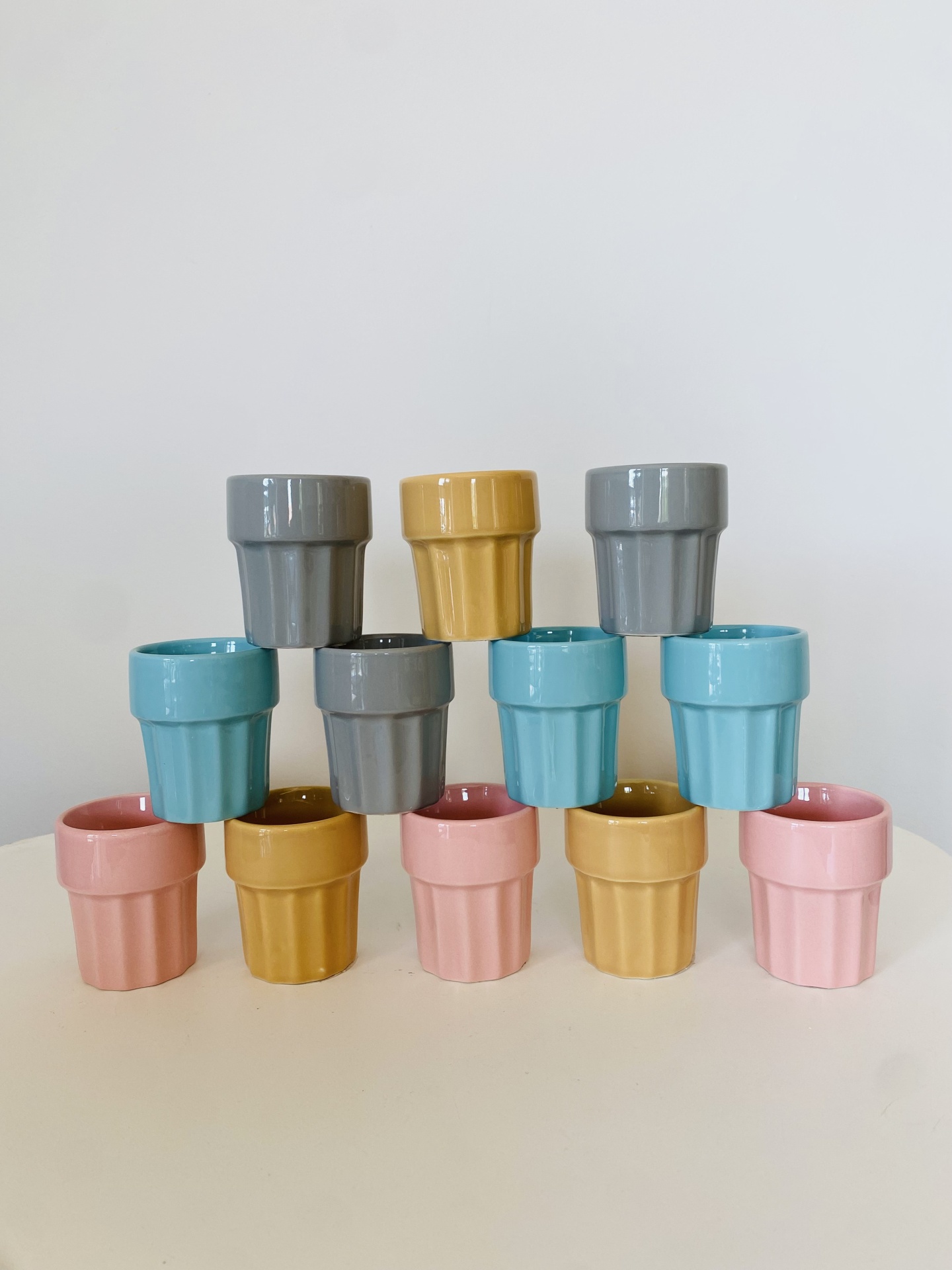 Doze copos de cerâmica coloridos empilhados em pirâmide sobre uma mesa branca