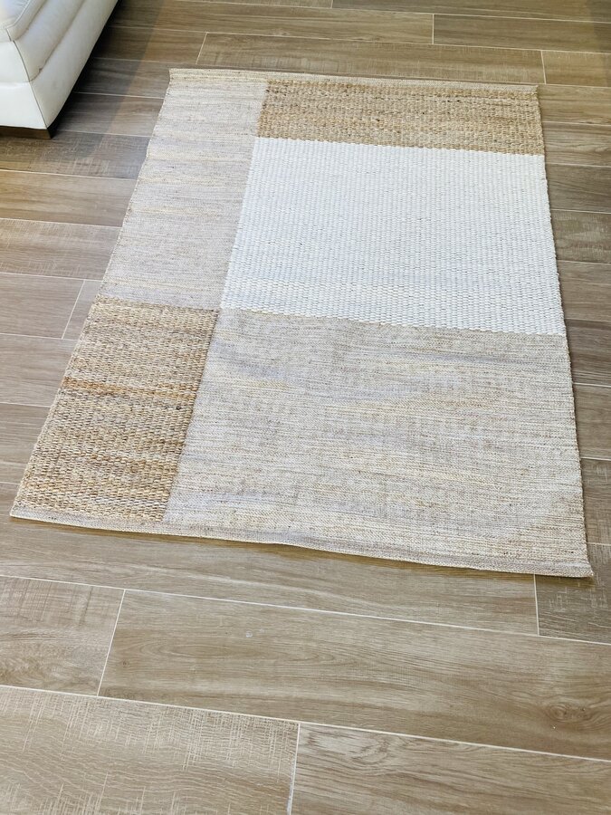 Tapete retangular com padrão em blocos bege, branco e castanho claro colocado sobre pavimento de madeira clara