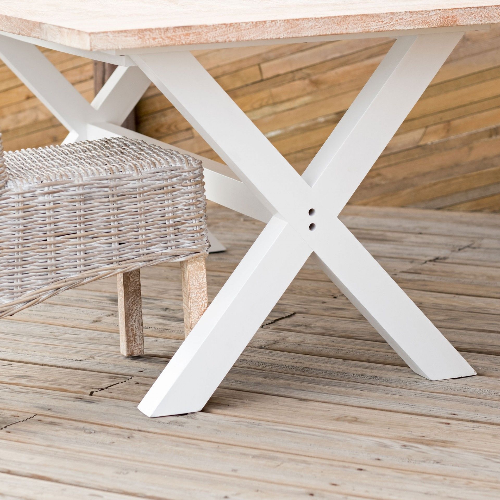 Mesa de madeira com pernas em X brancas e banco de fibra sintética cinzenta ao lado sobre piso de madeira