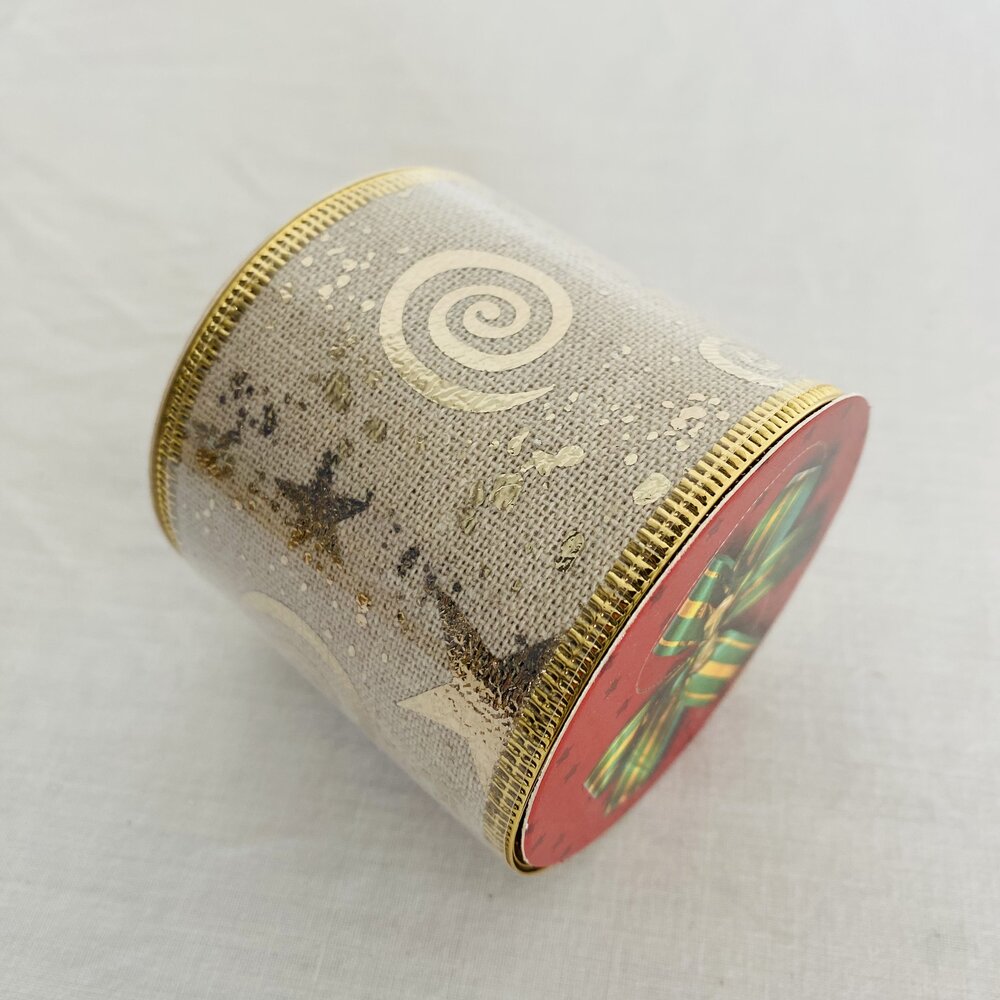 Lata decorativa cilíndrica com padrão de espirais e tampa vermelha com laço verde.