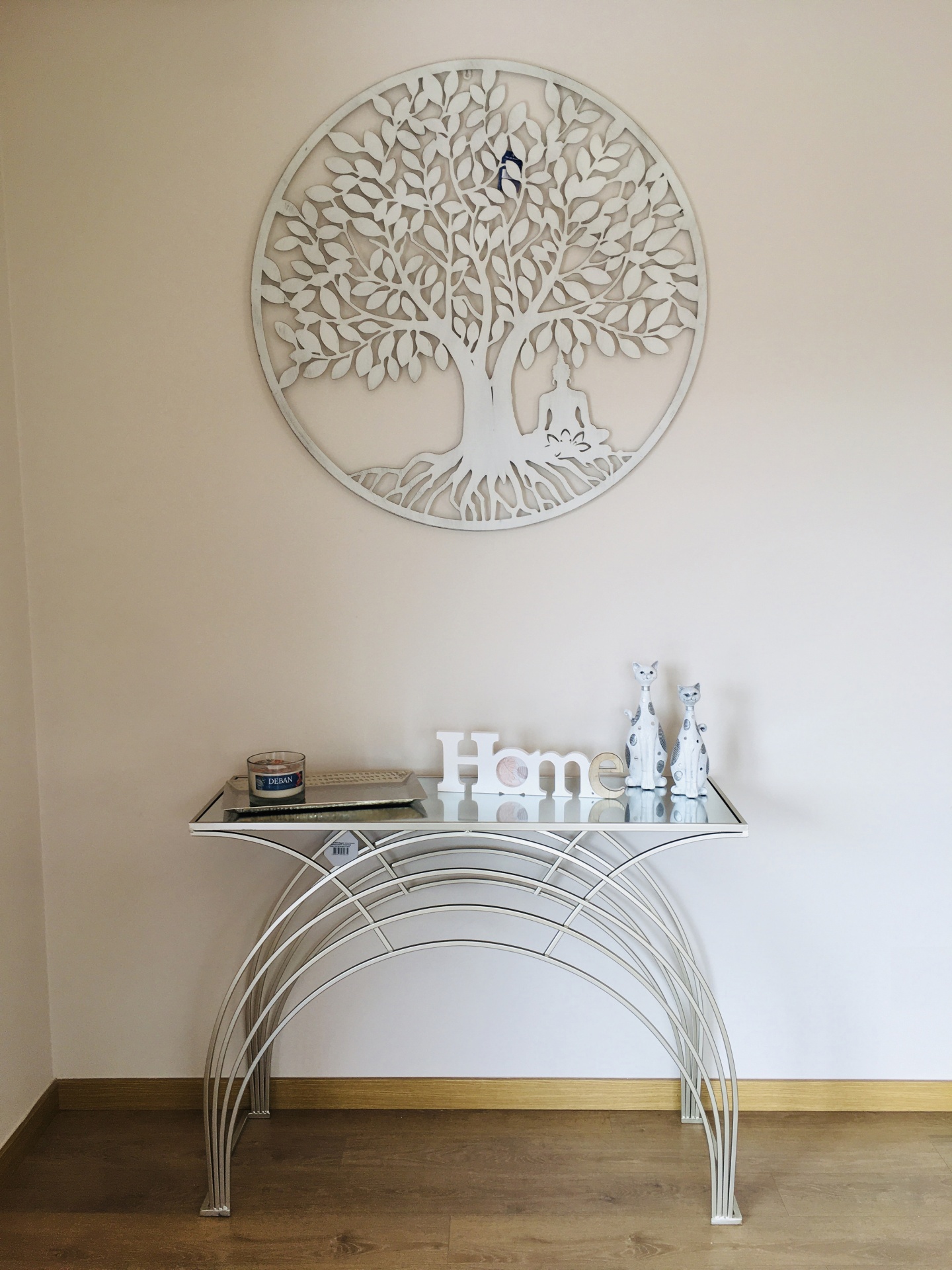 Consola decorativa branca com tampo de vidro e decoração com letras e estatuetas, painel de árvore na parede