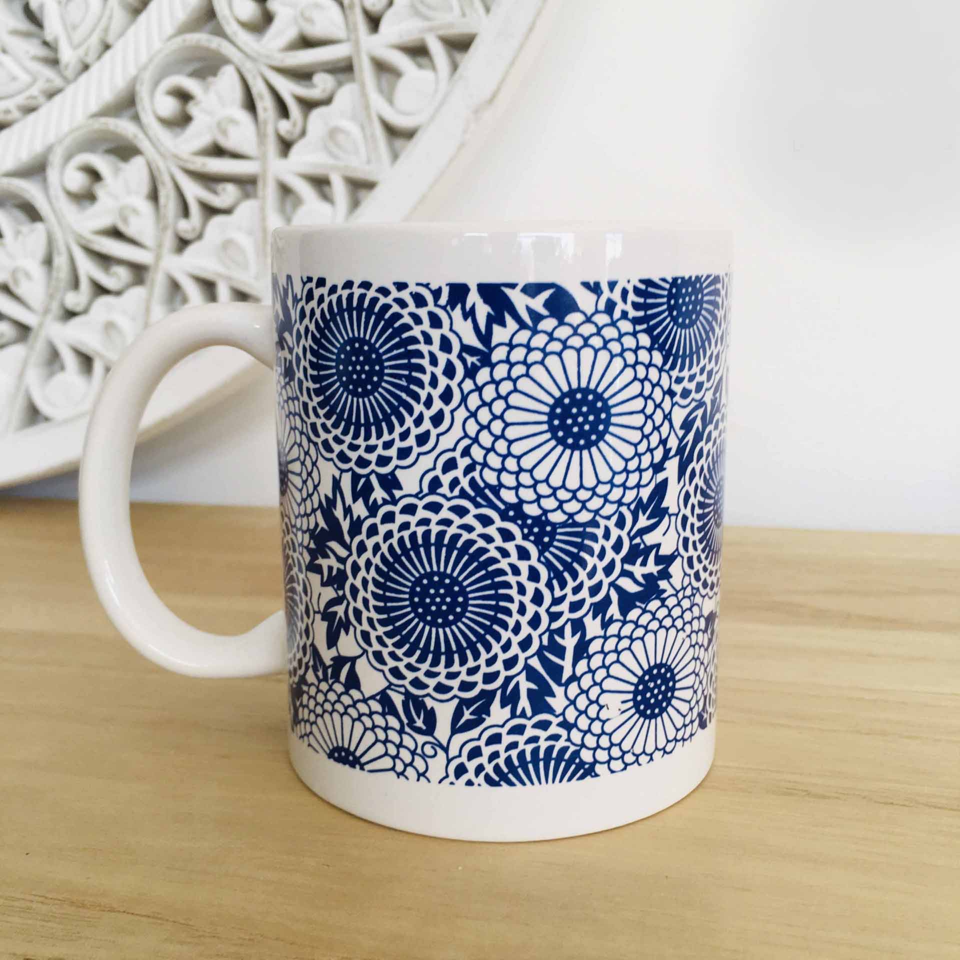 Caneca branca com padrão azul de flores sobre superfície de madeira