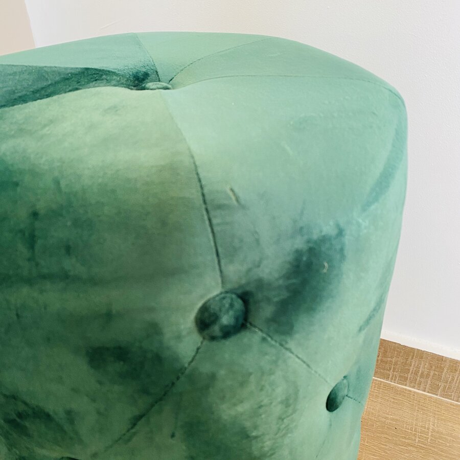 Pufe verde aveludado redondo com botões, chão de madeira clara e parede branca ao fundo