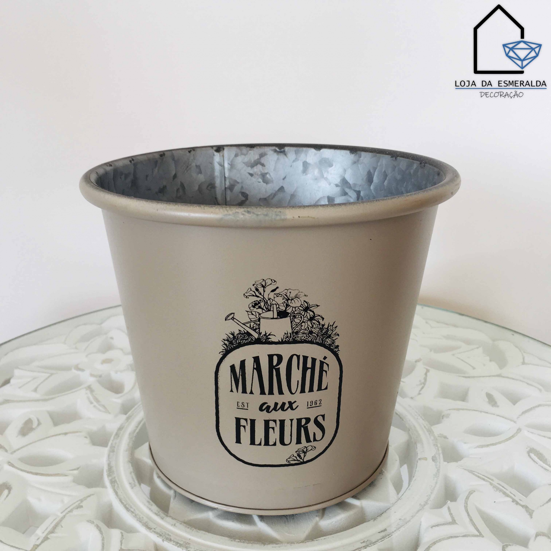 Vaso de metal bege com texto e ilustração de flores em mesa branca decorativa
