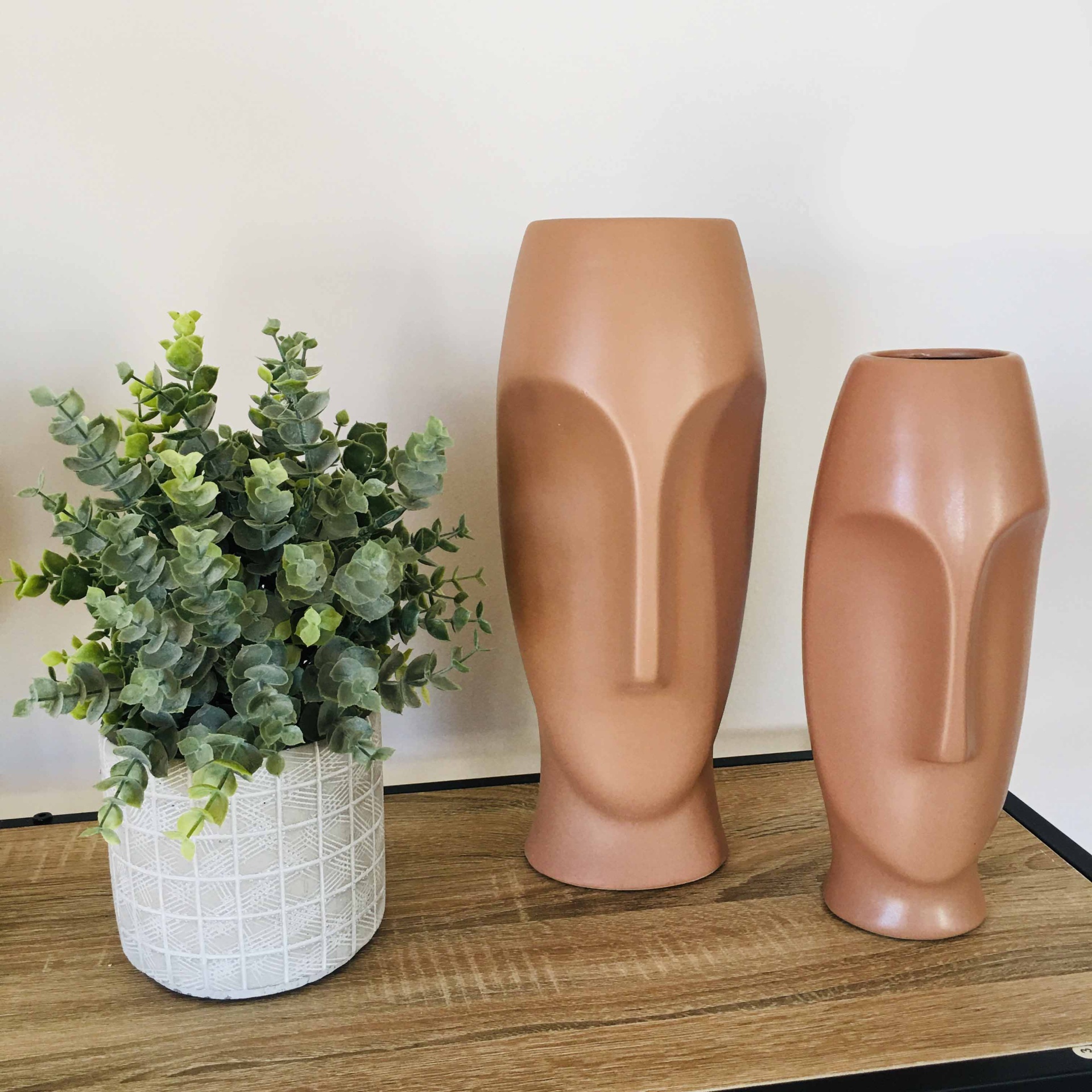 Três vasos decorativos de cerâmica e planta artificial sobre superfície de madeira