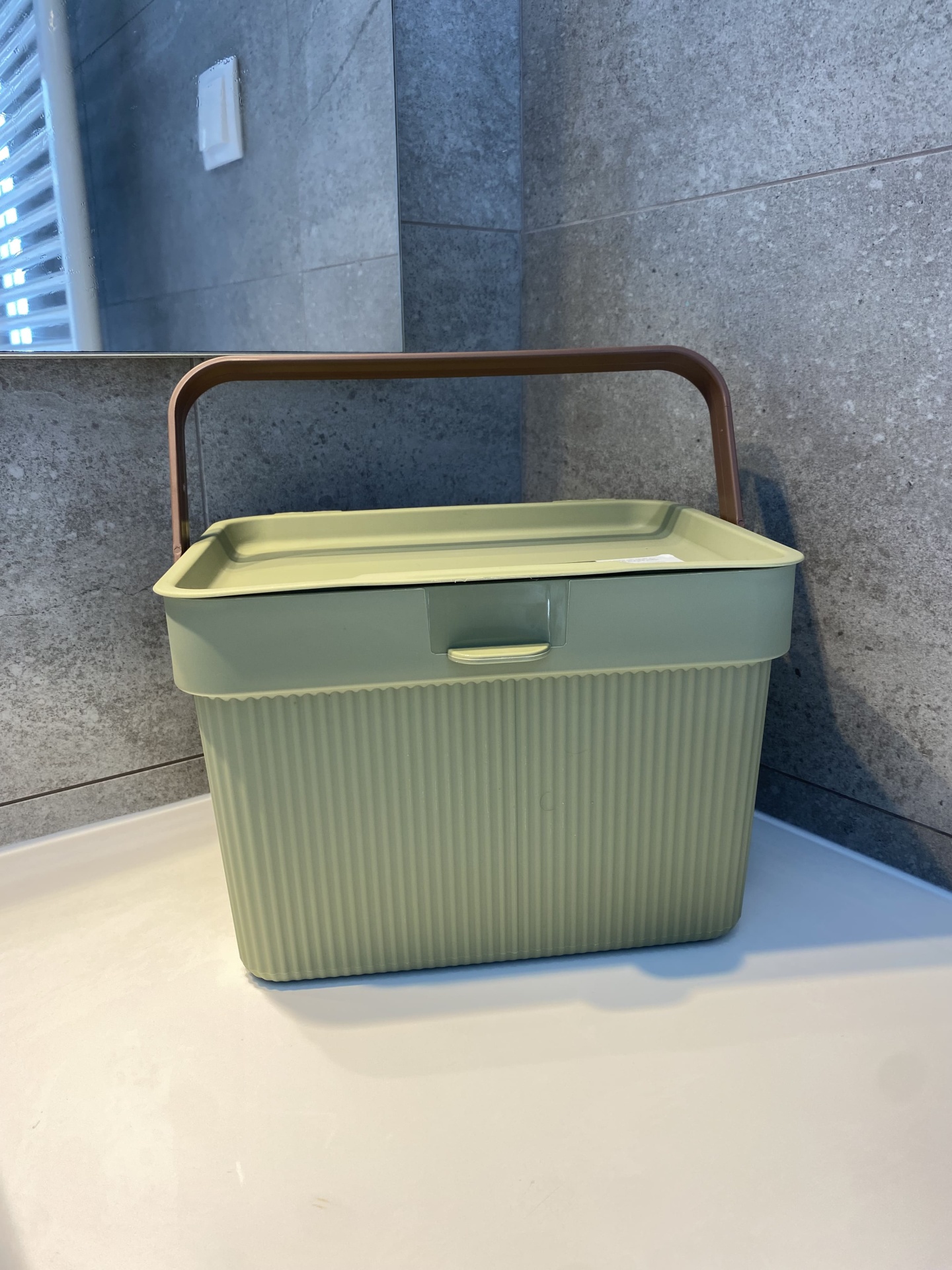 Caixa organizadora verde claro com pega castanha e textura canelada colocada numa superfície branca