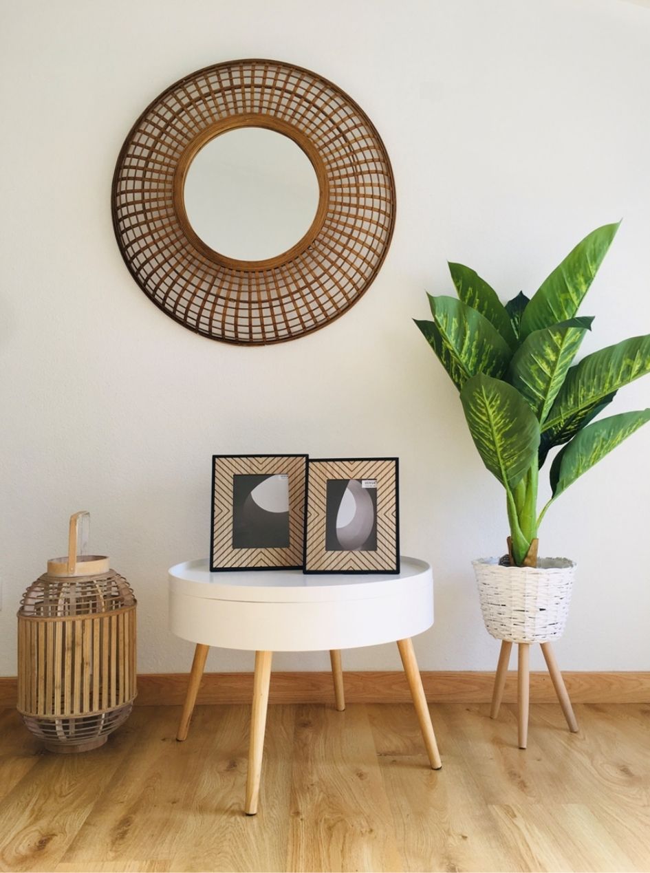 Espelho redondo de madeira, mesa branca com molduras e planta em vaso branco com suporte de madeira