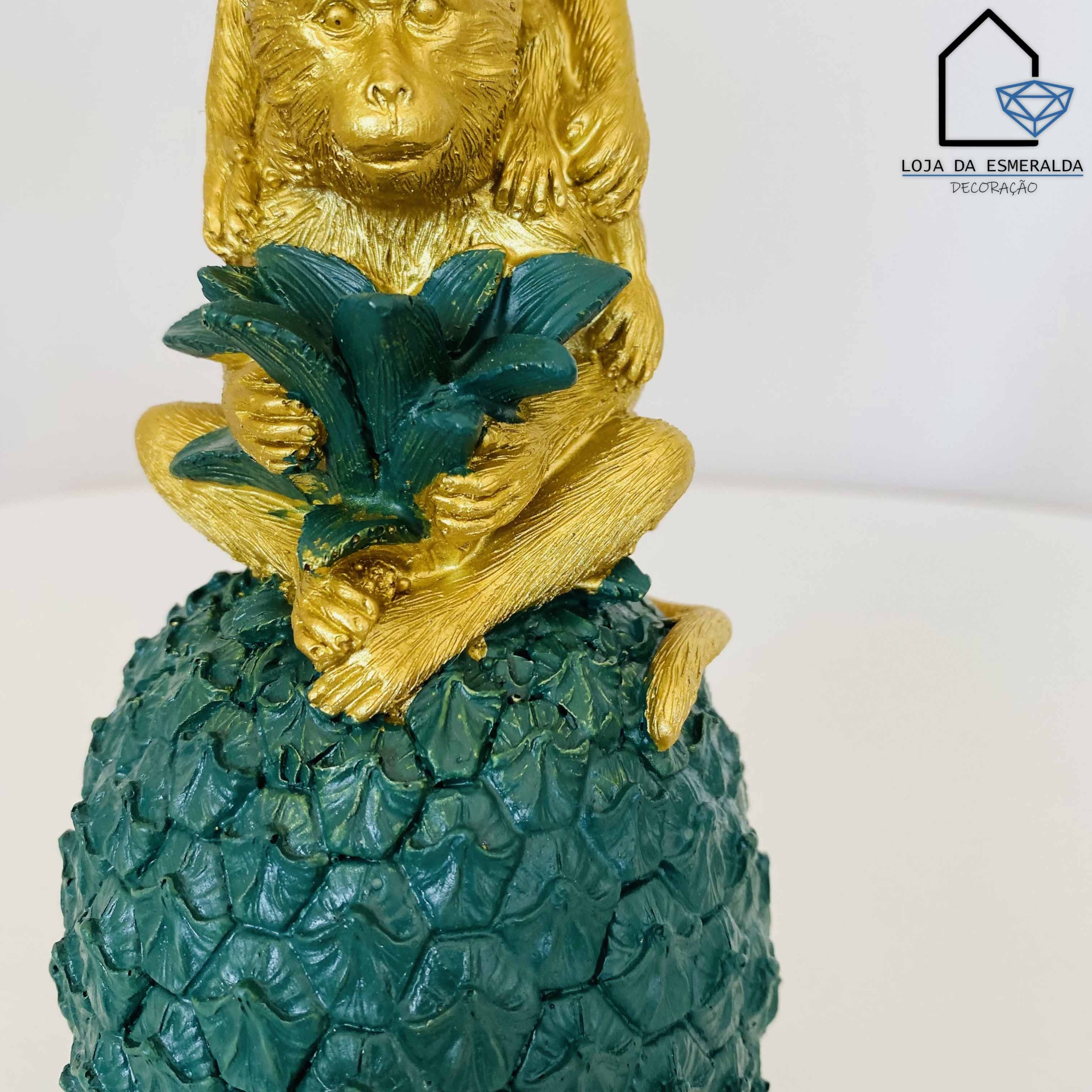 Estatueta dourada de macaco sentado num abacaxi verde texturizado com folhas na mão