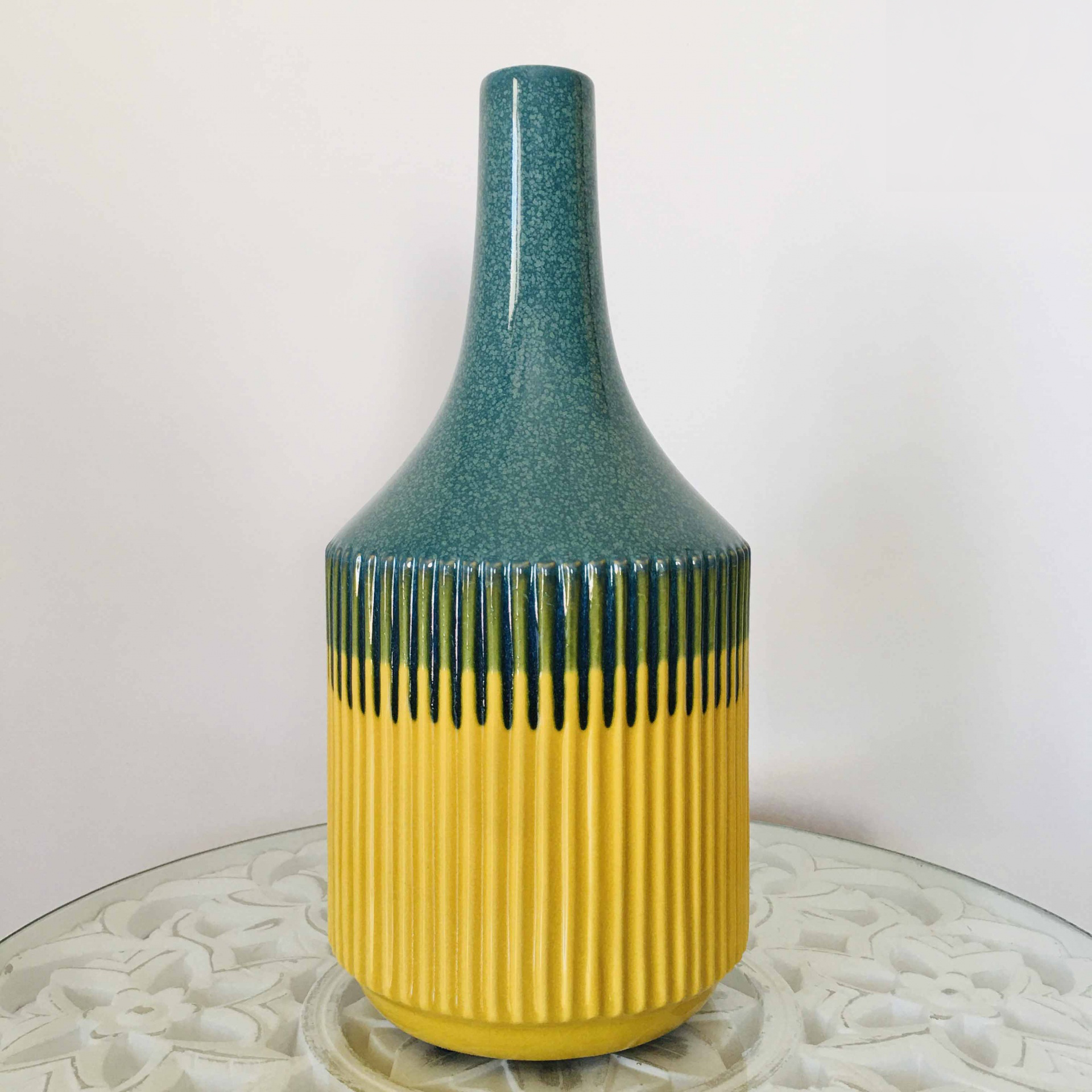 Vaso de cerâmica azul esverdeado e amarelo com padrão vertical sobre superfície branca decorada