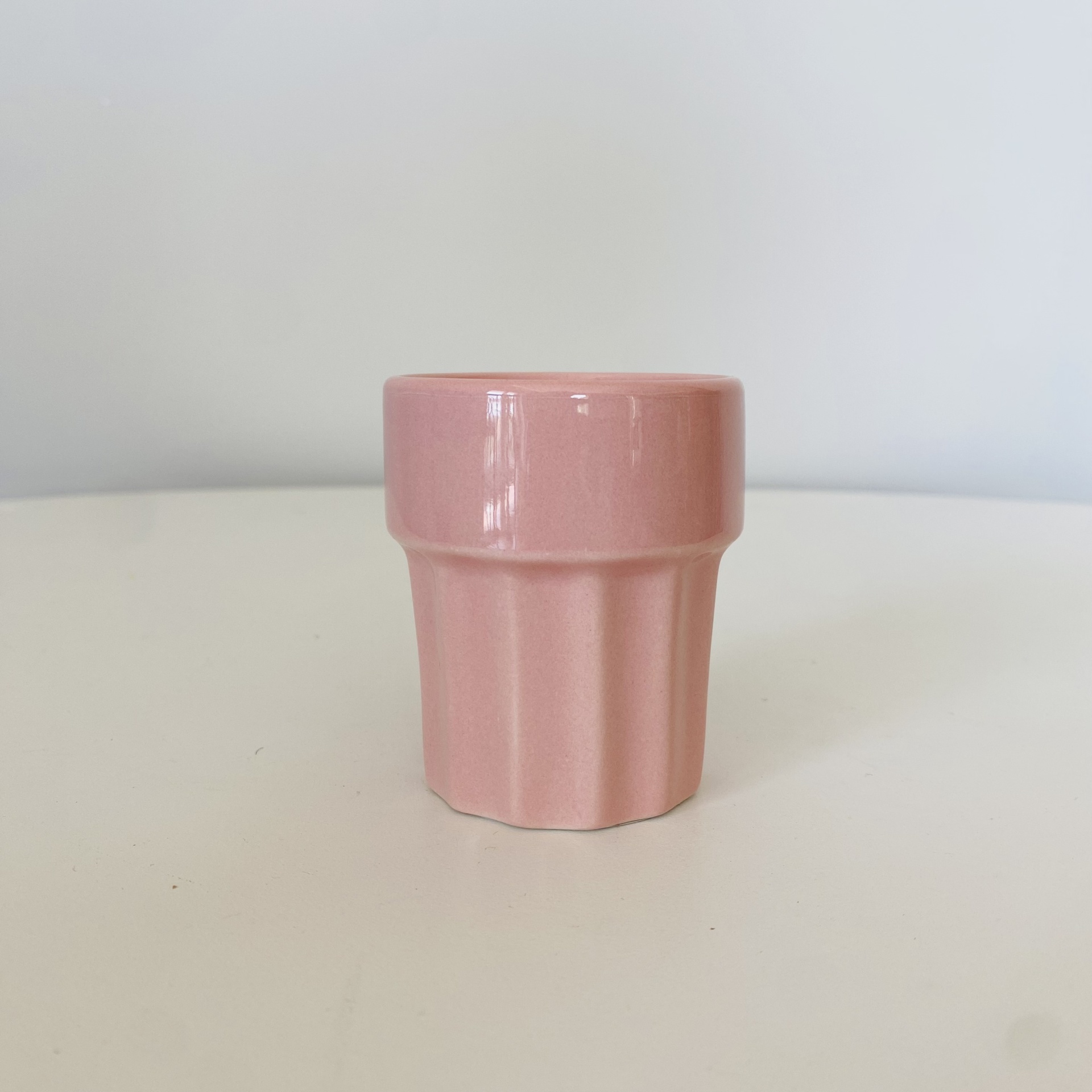 Copo pequeno de cerâmica rosa em superfície branca