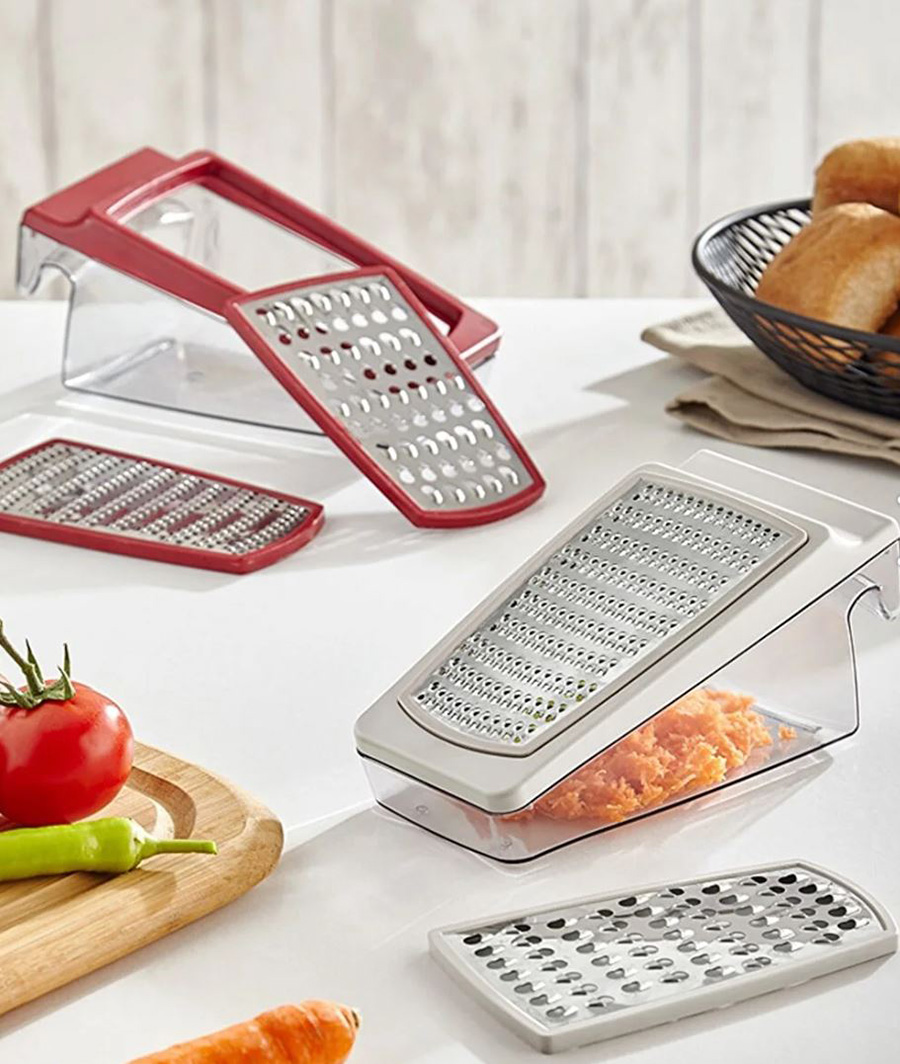 Raladores de cozinha em plástico e metal com recipientes transparentes e legumes numa mesa branca