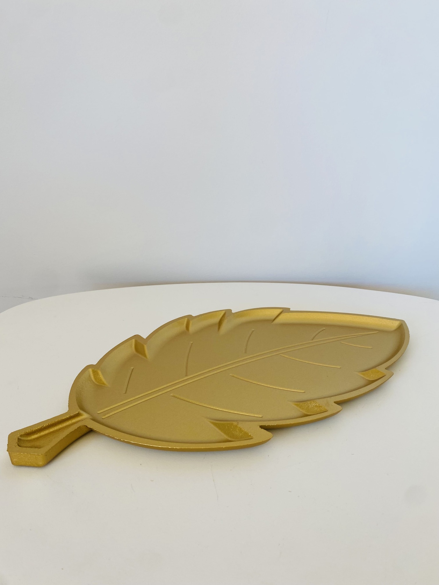 Tabuleiro decorativo dourado em forma de folha sobre mesa branca