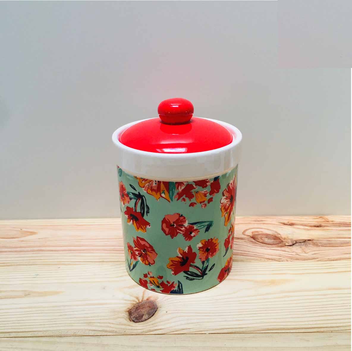Frasco cerâmico com tampa vermelha e padrão floral colorido em fundo verde.
