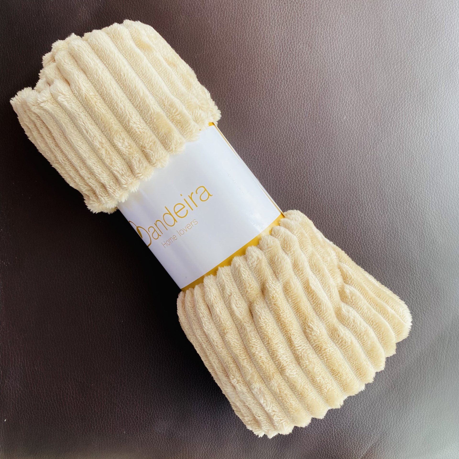 Manta bege clara canelada com etiqueta branca 'Bandeira' sobre superfície escura