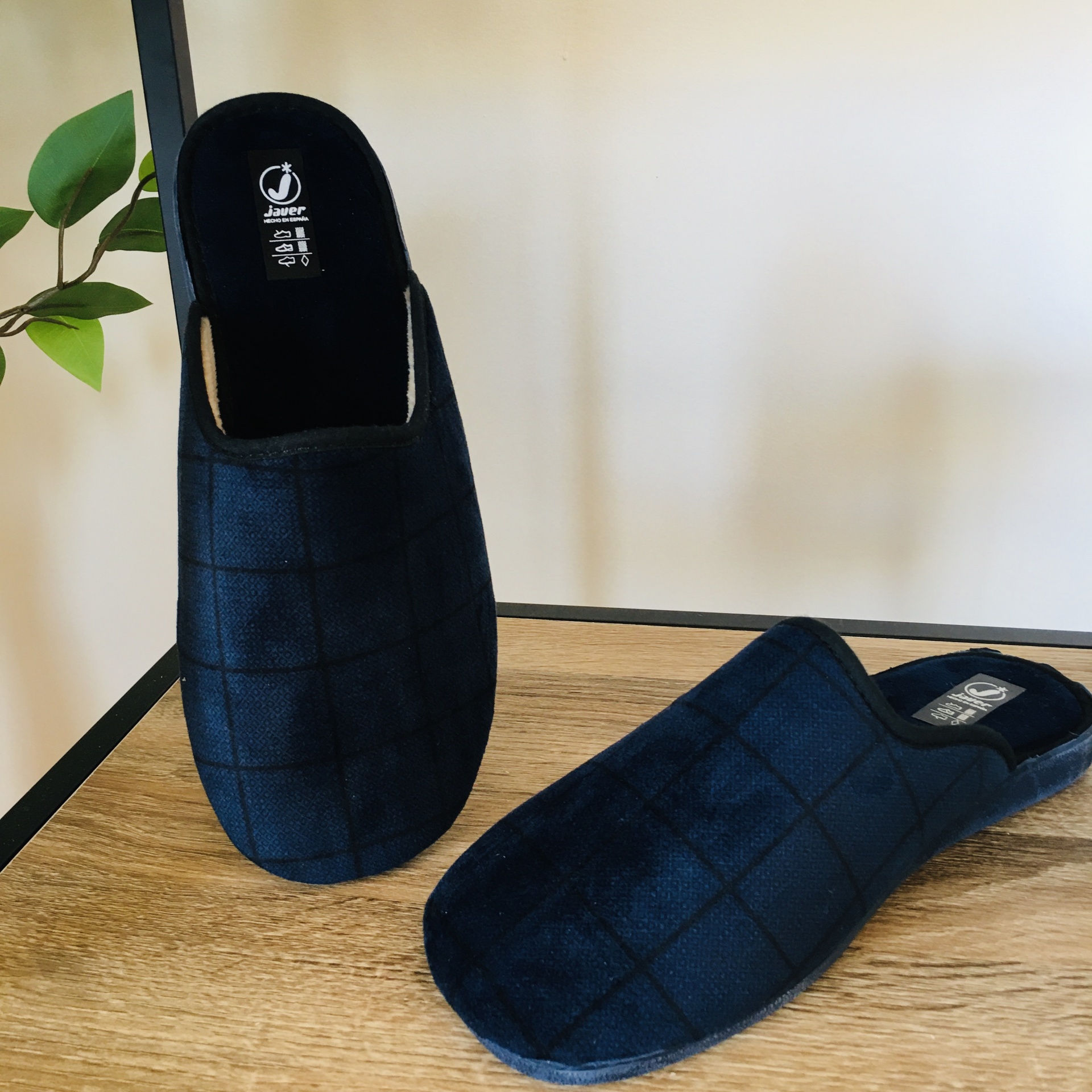 Chinelos masculinos pretos com padrão quadrado em fundo branco e superfície de madeira