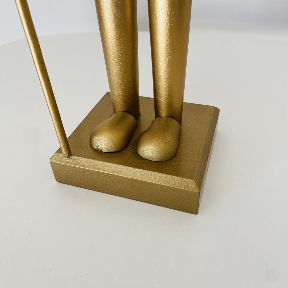 Estátua dourada decorativa sobre base quadrada em superfície branca