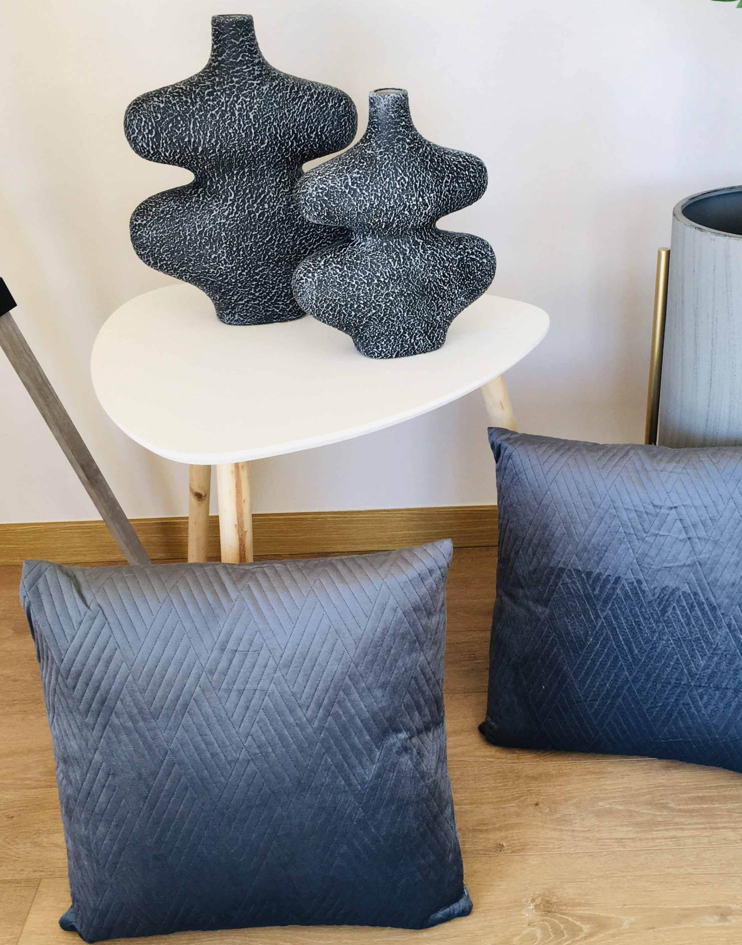 Almofadas pretas com padrão geométrico e esculturas abstratas pretas numa mesa branca