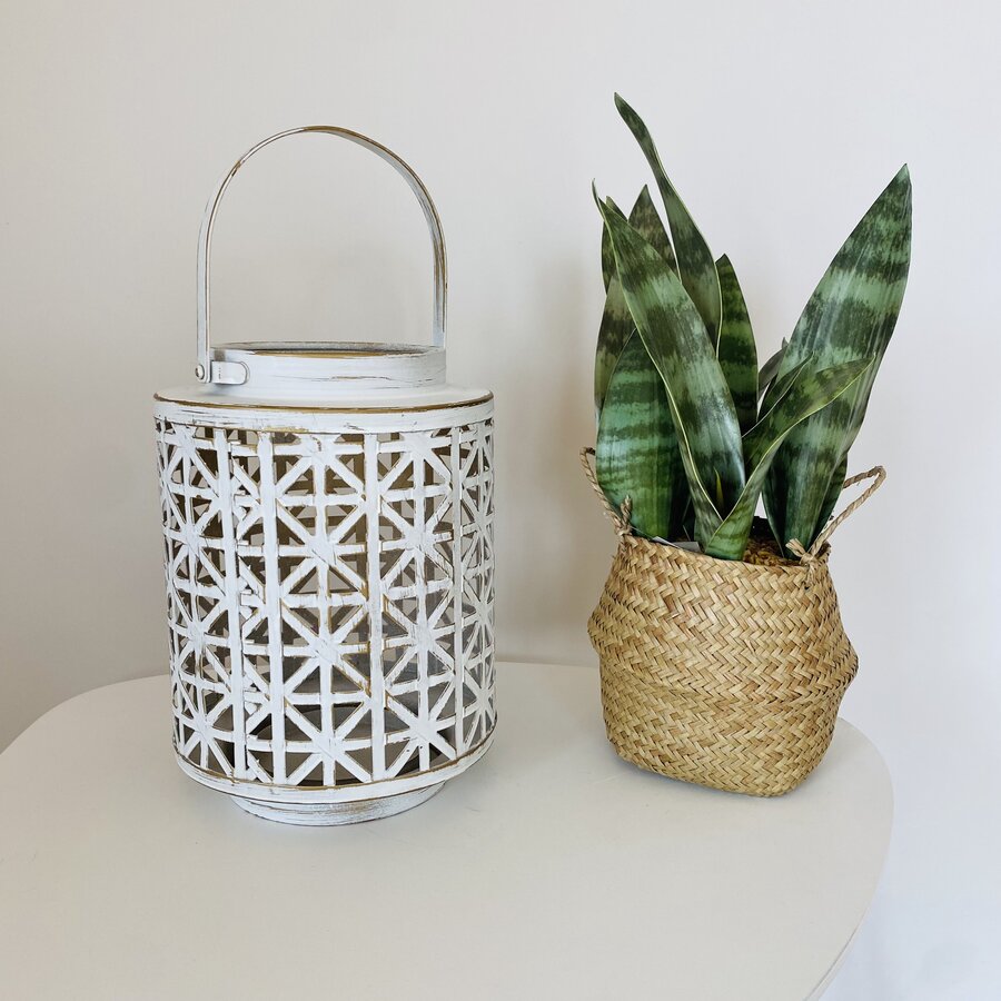 Lanterna branca em metal com padrão geométrico ao lado de planta em vaso de palha