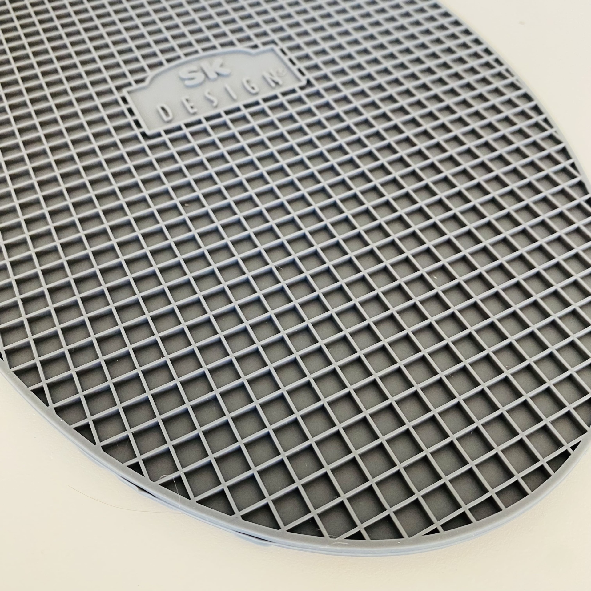 Base oval cinzenta com padrão de grelha e etiqueta SK DESIGN