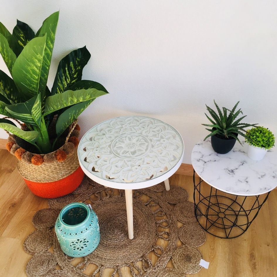 Mesa branca decorativa com detalhes florais ao lado de mesa com tampo de mármore e plantas em vaso sobre tapete de fibras