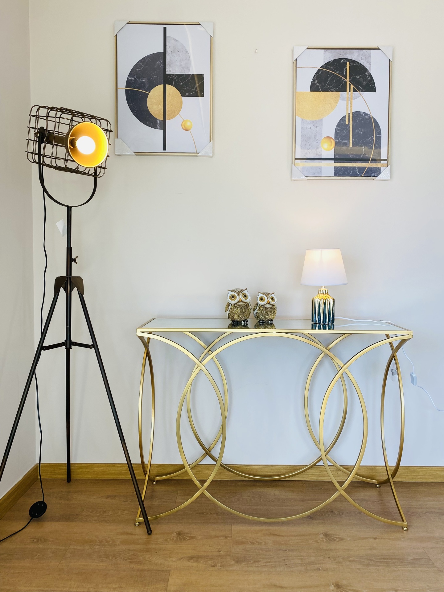 Consola dourada em sala com ornamentos, lâmpada de mesa, pinturas abstratas e candeeiro de pé