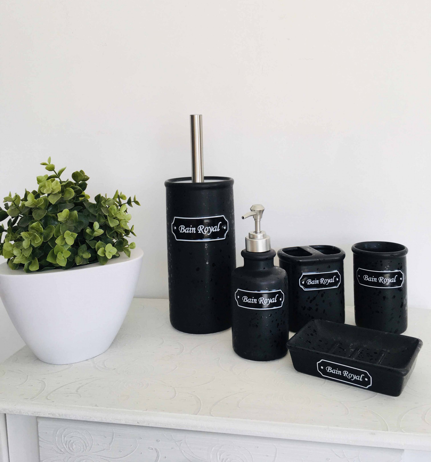 Conjunto de acessórios de casa de banho preto com etiqueta Bain Royal e planta em vaso branco sobre superfície branca