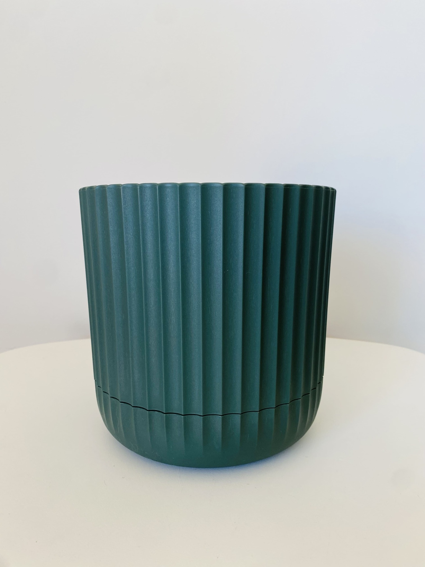 Vaso verde escuro estriado sobre mesa branca.