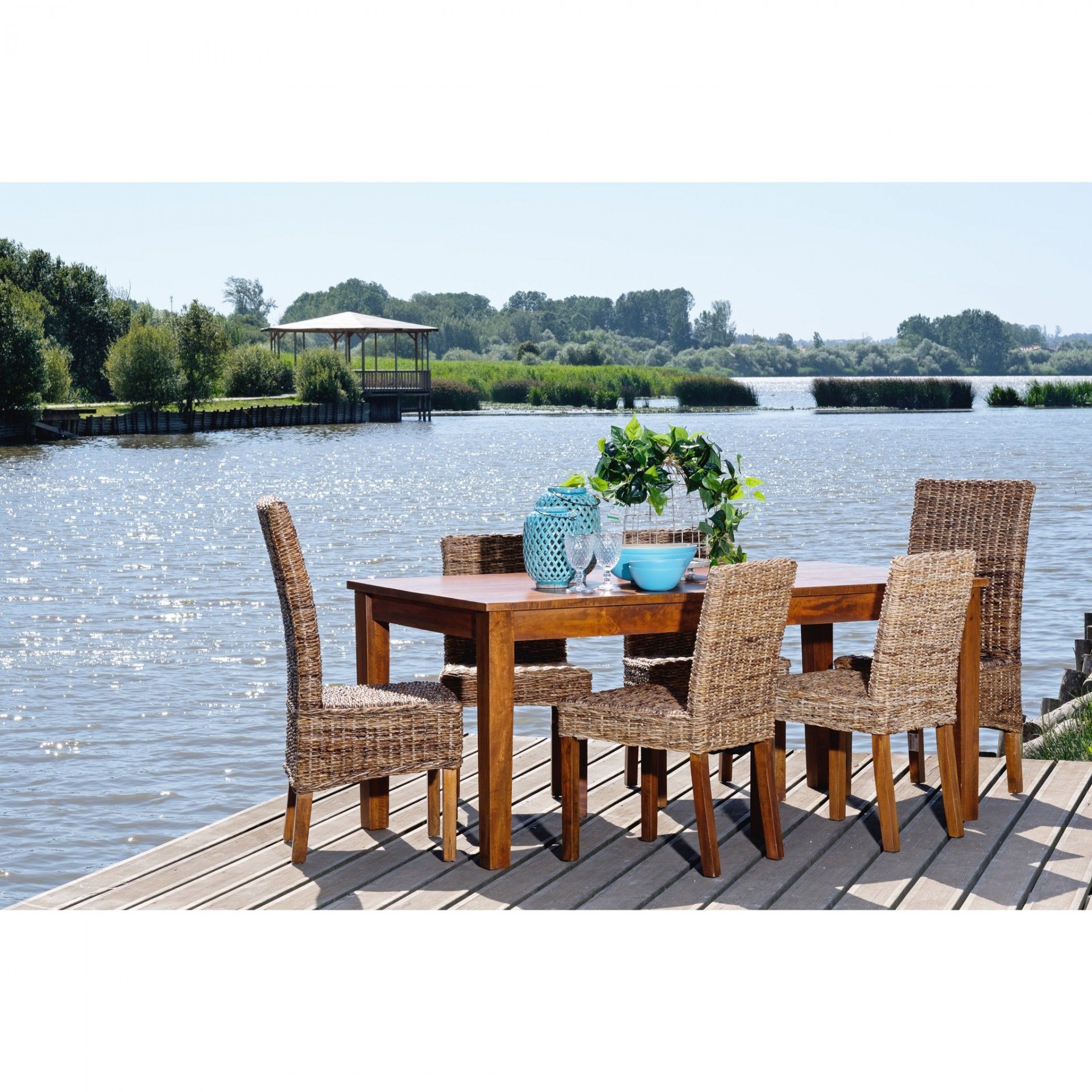 Conjunto de mesa e cadeiras de madeira e rattan natural numa plataforma de madeira perto da água