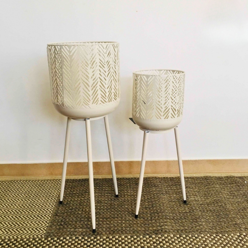 Dois vasos metálicos creme com suporte de pernas longas em tapete padrão geométrico