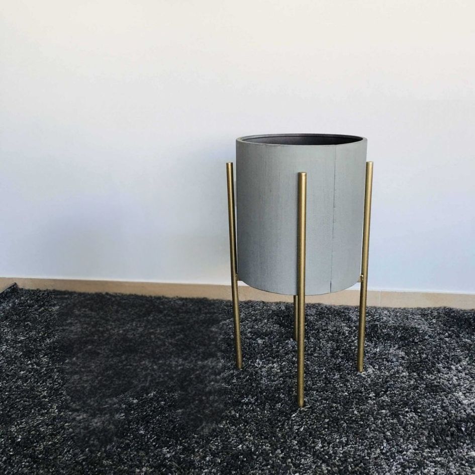 Vaso cinza com suporte metálico dourado num tapete cinza escuro