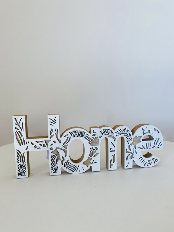 Objeto decorativo de madeira branco com a palavra Home recortada com padrão de folhas