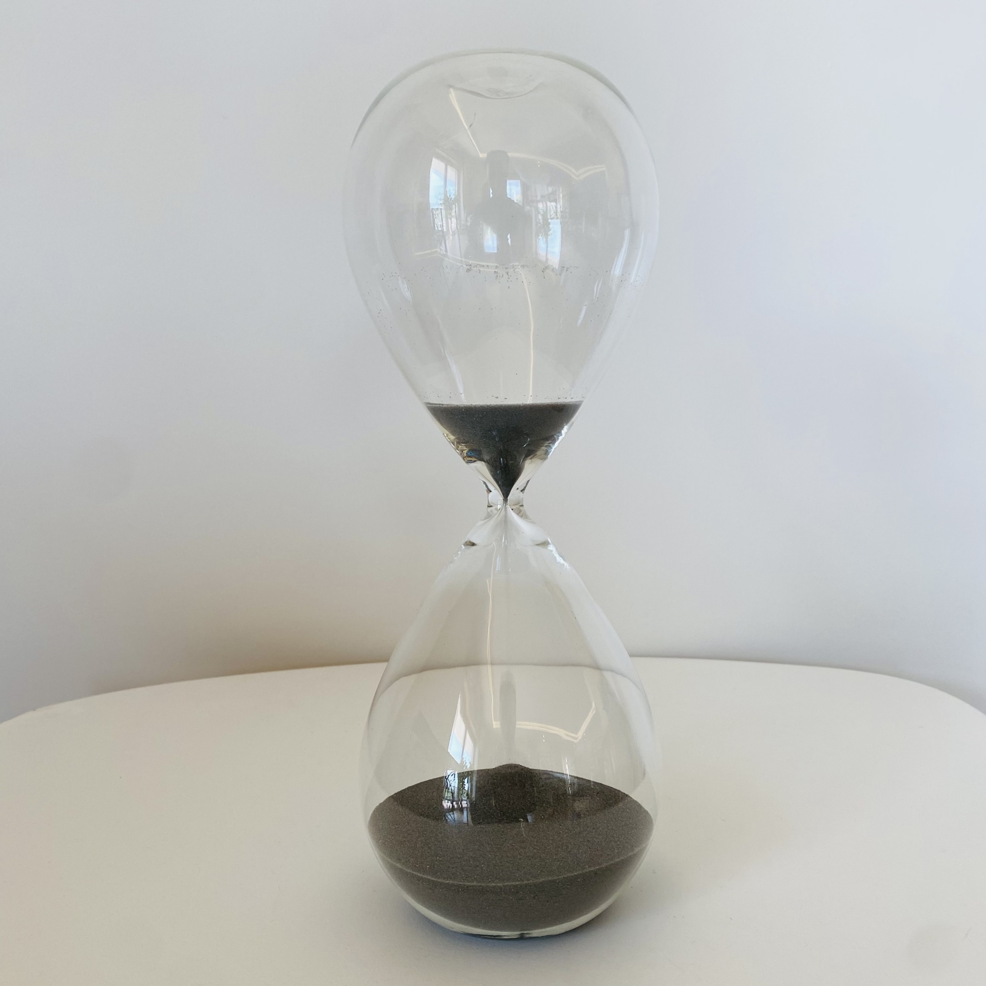 Ampulheta de vidro com areia preta sobre superfície branca